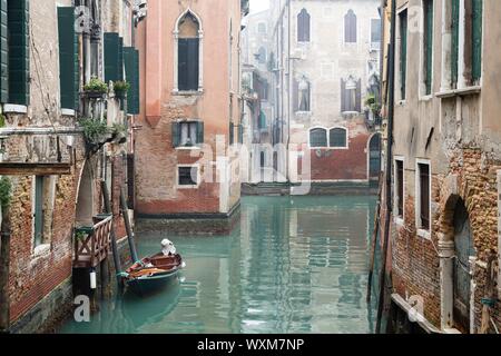 Venice canal scene depicting a small boat in a quiet residential part of Venice in winter on a cool misty day with no people or tourists Stock Photo