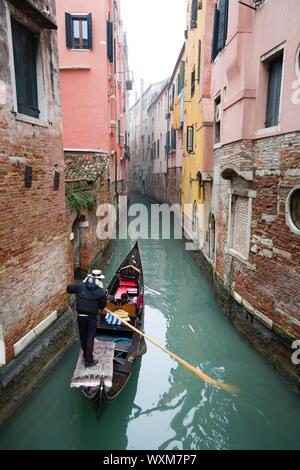 A gondolier takes tourists on a gondola ride down a quiet narrow canal through Venice in winter Stock Photo