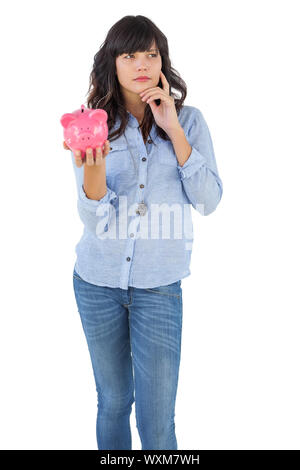 Thinking young woman holding her piggy bank on white background Stock Photo