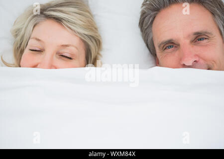 Couple waking up under the covers at home in bed Stock Photo