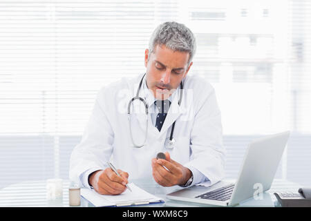 Doctor holding medication and writing a prescription at medical office Stock Photo