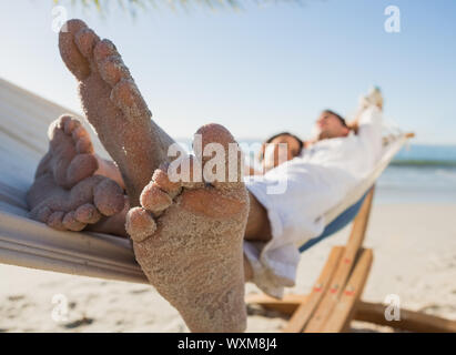 Close up of sandy feet of couple in a hammock on the beach Stock Photo
