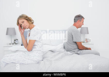 Annoyed couple sitting on different sides of bed having a dispute with woman looking at camera in bedroom at home Stock Photo