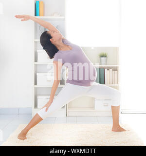 Prenatal yoga class. Full length healthy 8 months pregnant calm Asian woman meditating or doing yoga exercise at home. Relaxation and stretching. Stock Photo