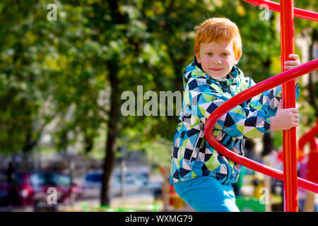Child playing on outdoor playground. Fashion kids play on school or kindergarten yard. Pretty boy. Cute boy in spring-autumn clothes. Red-haired Stock Photo