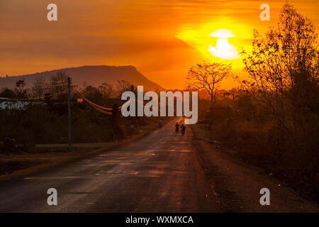 Motorbike silhouette driving on a scenic road in orange sunset in countryside of Laos Stock Photo