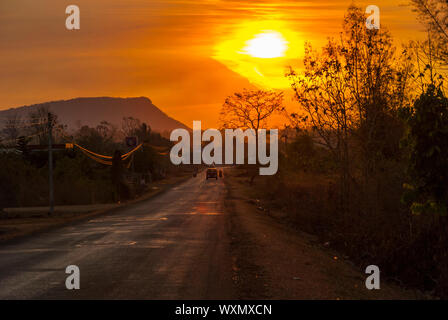 Car and motorbike silhouette driving on a scenic road in orange sunset in countryside of Laos Stock Photo