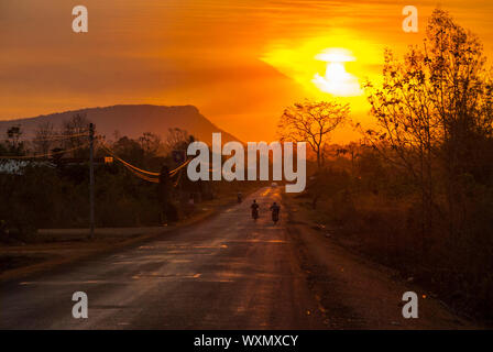 Motorbike silhouette driving on a scenic road in orange sunset in countryside of Laos Stock Photo
