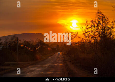 Car and motorbike silhouette driving on a scenic road in orange sunset in countryside of Laos Stock Photo