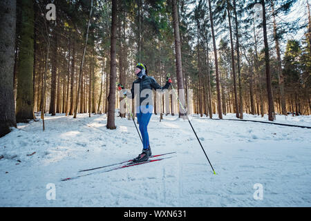 Cross-country skiing woman doing classic nordic cross country skiing in trail tracks in snow covered forest. Training track for skiers in the park of Stock Photo