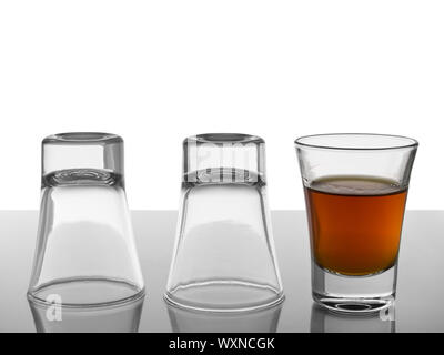 Two empty shots upside down and a third one full of liquor. Stock Photo