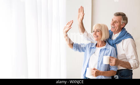 Happy senior couple looking through window and hugging Stock Photo