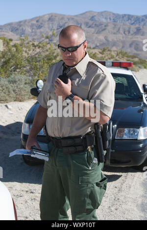 Policeman using walkie talkie near police car Stock Photo