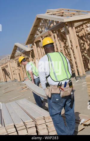 Two construction workers carrying wooden plank on site Stock Photo