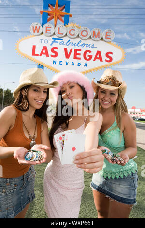 Women holding cards and gambling chips in front of Las Vegas welcome sign, Nevada, USA Stock Photo