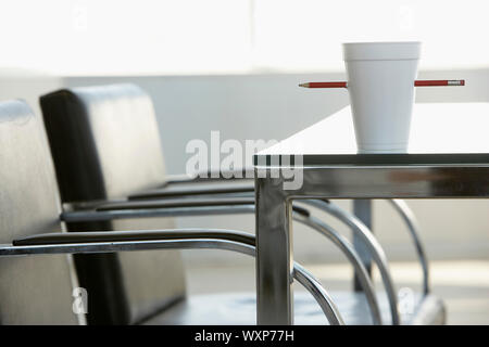 Disposable cup pierced by pencil on table in conference room Stock Photo