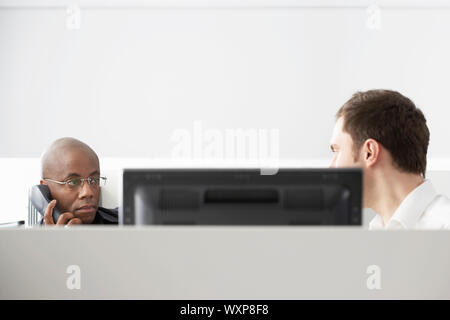 Two office workers sitting in office cubicle one using phone Stock Photo