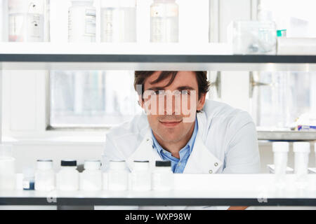 Portrait of confident male scientist looking through shelves in laboratory Stock Photo