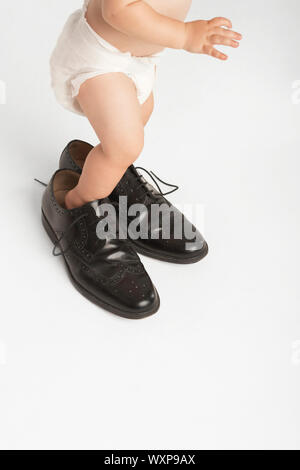 Low section of baby wearing man's shoes isolated on white background Stock Photo