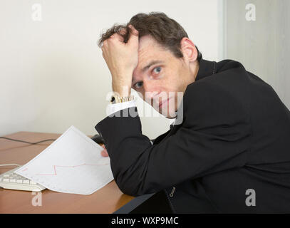 Sorrowful man at the office, on a workplace with graph Stock Photo