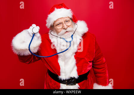 Worried calm Santa look at camera hold stethoscope in hand stand isolated on bright red background Stock Photo