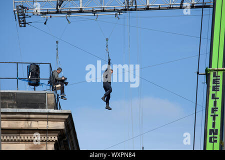 Rooftops, West College Street, Edinburgh, Scotland, UK. 17th September 2019. Clear weather sunshine and blue skies for filming for 'Fast and Furious 9', pictured, film cameraman and stunt actor suspended in mid air from a gantry which they zip wire pulley over while attached to a massive crane, as this scene continued for a second day above the city centre streets. Stock Photo