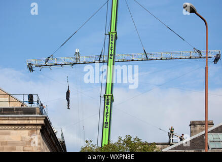 Rooftops, West College Street, Edinburgh, Scotland, UK. 17th September 2019. Clear weather sunshine and blue skies for filming for 'Fast and Furious 9', pictured, film cameraman and stunt actor suspended in mid air from a gantry which they zip wire pulley over while attached to a massive crane, as this scene continued for a second day above the city centre streets. Stock Photo
