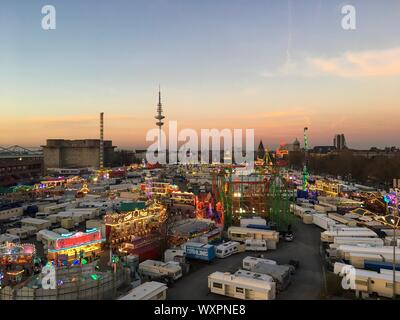 HAMBURG - March 27, 2017: Wide Bird's Eye View of large Fun Fair 'Hamburger Dom' with Roller Coaster, Carnival Rides and Hamburg Skyline at dusk Stock Photo