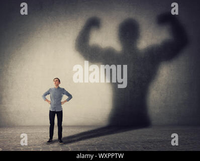 Brave teenager boy facing his fears as a powerful hero. Guy casting a strong muscular bodybuilder shadow, showing big biceps. Self defense, inner stre Stock Photo