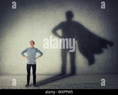 Casual teenage, keeps arms on hips smiling confident, casting a superhero with cape shadow on the wall. Student ambition success concept. Leadership h Stock Photo