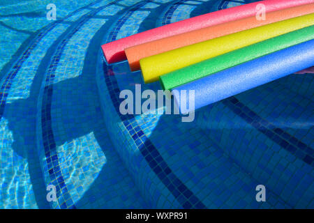 Rainbow coloured pool noodles floating in a swimming pool, summer fun Stock Photo