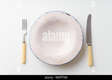 Handmade ceramic empty plate with knife and fork on white background Stock Photo