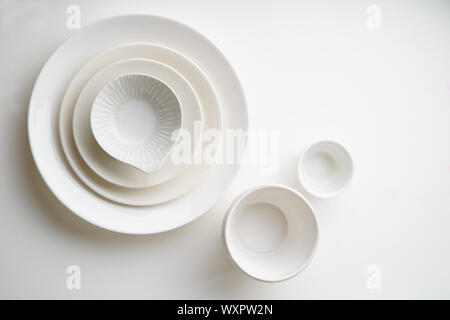 Porcelain plates of various form and size on white background. Overhead image, copy space. Stock Photo