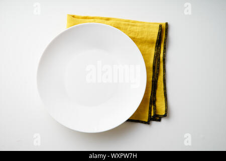 White empty plate with yellow textile napkin on white background Stock Photo
