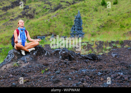 Young woman travel in Bali island. Active girl relaxing in yoga meditating pose during trekking to Batur volcano. Walking day tour, mountain hiking ac Stock Photo