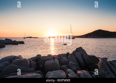 Two yachts moored in a bay as the sun sets over the Mediterranean sea and large granite boulders on the coast of Cavallo Island in the Lavezzi archipe Stock Photo