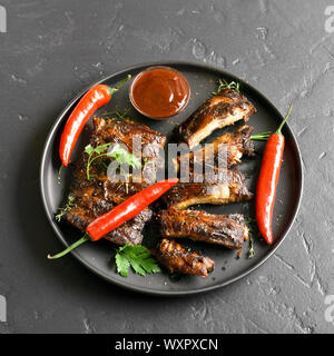 Spicy grilled spare ribs on plate over black stone background. Tasty bbq meat. Stock Photo