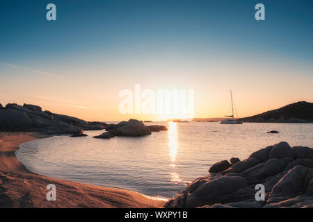 Yacht moored in a bay as the sun sets over the Mediterranean sea and large granite boulders on the coast of Cavallo Island in the Lavezzi archipelago Stock Photo