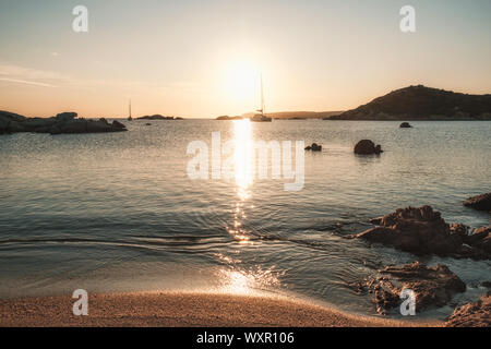 Two yachts moored in a bay as the sun sets over the Mediterranean sea and large granite boulders on the coast of Cavallo Island in the Lavezzi archipe Stock Photo