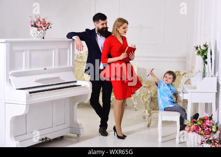 Kid growthing in welfare. Parents enjoying parenthood, carefree, happy. Mother and father stands near piano, watching while their son on busy face dra Stock Photo