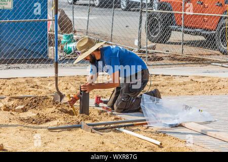 HICKORY, NC, USA-13 SEPT 2019: Young male construction worker installing and leveling an electrical outlet box in a town square.  Close up image. Stock Photo