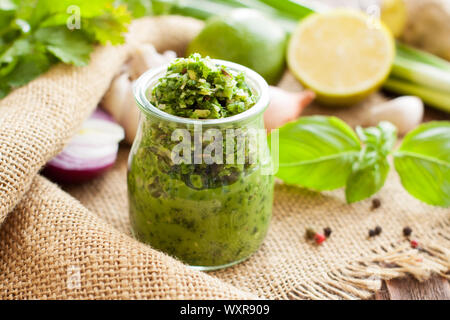 Green sauce in a glass jar in background with basil, lime, onion and parsley. Thai green curry paste Stock Photo