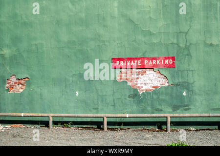 A colorful vintage wall marked "Private parking" with green stucco, some of which has peeled showing the original bricks underneath, in Wallace, Idaho Stock Photo
