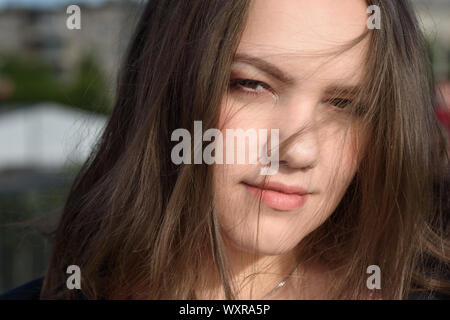 Portrait of brunette girl. Girl in black jacket with long hair on the street in summer day. Plus size model Stock Photo