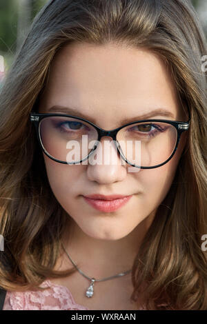 Portrait of brunette girl with glasses. Girl in black jacket with long hair on the street in summer day. Plus size model Stock Photo
