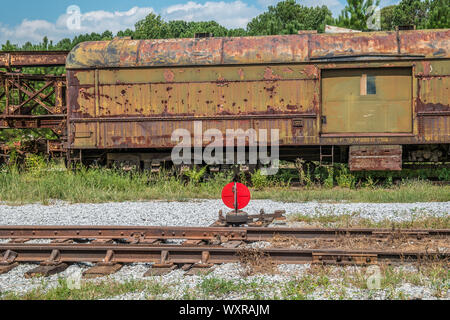 On exempt train tracks sits an old vintage abandoned railroad boxcar covered in weeds alongside a track switcher on a sunny day Stock Photo