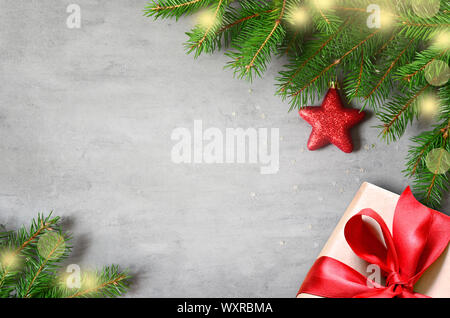Christmas presents with red ribbon on gray background in a frame made of fir branches with star. Flat lay, top view. Christmas background. Stock Photo