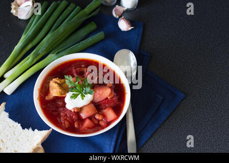 Traditional Ukrainian and Russian cuisine, soup cooked with beets and tomatoes. A white plate with beetroot soup on dark background. Stock Photo