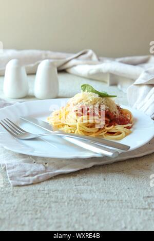 Pasta Fettuccine Bolognese with tomato sauce on white plate. Carlic and salt and tomatoes on a concrete background with linen napkins. Stock Photo