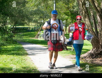 A couple walking thru the park. He wears a traditional Gaelic kilt, she wears a life jacket (the Dragon Boat Festival celebrations 2019).. Stock Photo